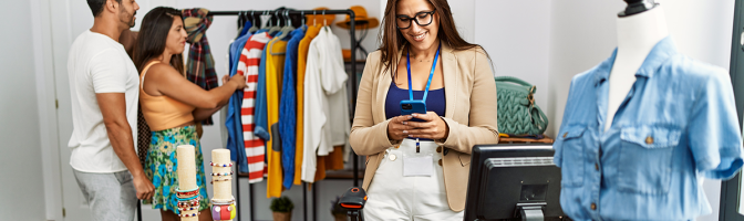 Shopkeeper woman smiling happy and using smartphone. Young couple shopping in the background. 