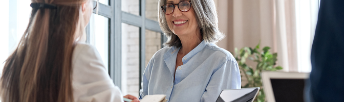 Happy mature businesswomen talking to colleague in meeting working together in office