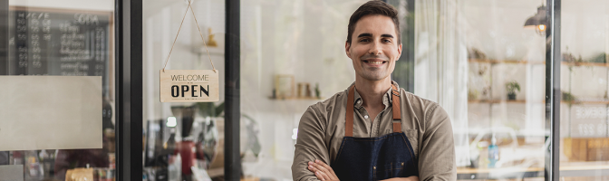 A male cafe employee standing in front of the store greets customers and has a sign that says open to show that the shop is open,