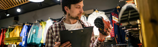 Store manager near shelves with hiking boots makes check list